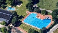 Freibad Mettingen Gesamtansicht Blick von oben auf das Gelände des Freibads Mettingen. Große Rasenflächen und zwei Schwimmbereiche. Umrahmt von großen Bäumen. Links ist das Hallenbad zu sehen.