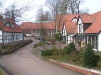 Außenansicht auf den Mettingen Schultenhof. Links und rechts sind Fachwerkhäuser in der Mitte ein gepflasterter Platz mit Büschen und einer Treppe