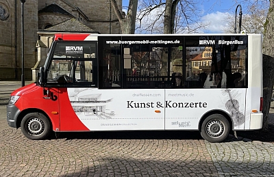 Bürgermobil Mettingen Ein Bild des Bürgermobil Mettingen. Seitenansicht. Der Kleinbus hat große Fenster und ist Weiß mit etwas Rot lackiert.