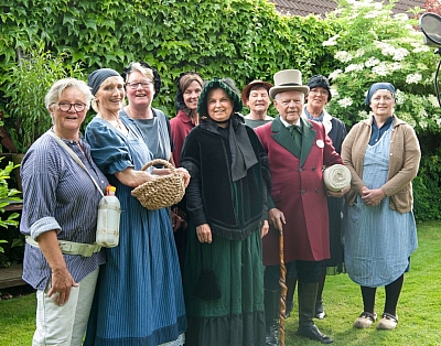 Gruppenfoto zum Mettinger Heimatlied Die Sänger und Musiker für das Mettinger Heimatlied stehen vor einem Mikrofon im Garten. Sie sind in traditioneller Kleidung und lächeln in die Kamera.
