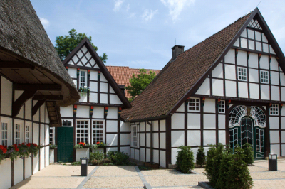 Mettinger Tüöttenmuseum Außenansicht auf schöne Fachwerkhäuser mit weißer Front, roten Blumen und hohen Dächern. Die Sonne scheint.